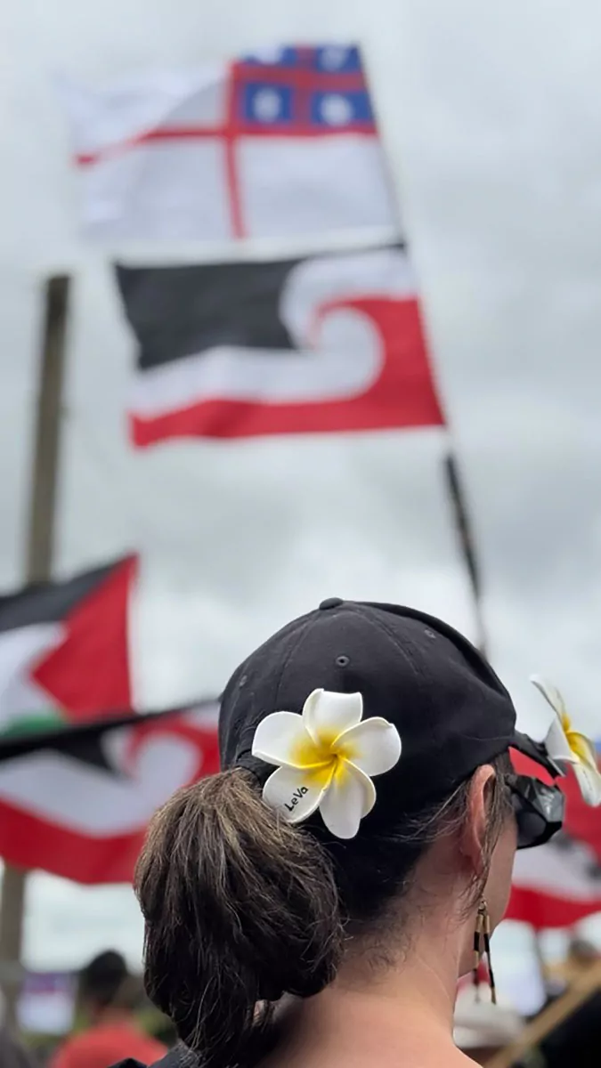 A Le Va sei on a woman's cap with Tino Rangatiratanga flags in the background