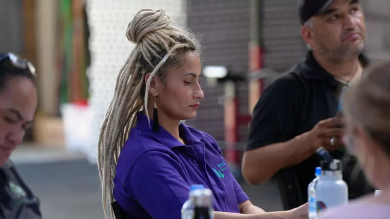 Woman with long bleached dreadlocks and purple shirt reading at a desk