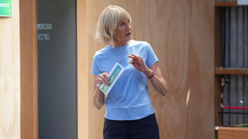 Woman in blue t-shirt standing and speaking, holding a name tag