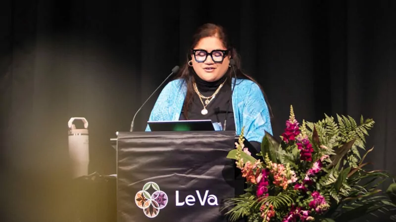 End Game speaker Nalei Taufa speaking at a lectern wearing a blue jacket and glasses